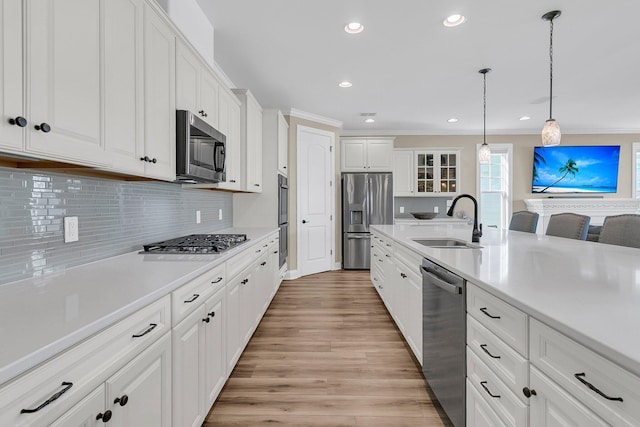 kitchen with light countertops, a sink, light wood finished floors, white cabinetry, and stainless steel appliances