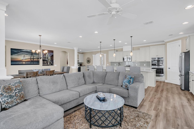 living room featuring visible vents, light wood finished floors, ornamental molding, decorative columns, and ceiling fan with notable chandelier