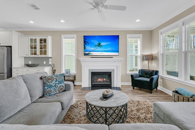 living room featuring light wood-type flooring, baseboards, visible vents, ceiling fan, and ornamental molding