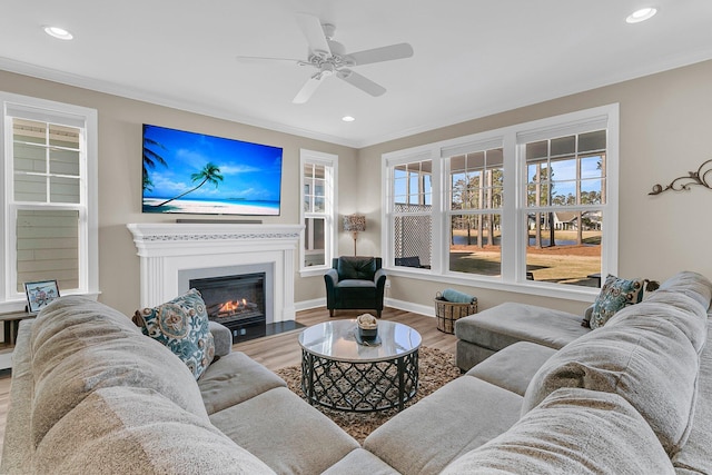living room with recessed lighting, ornamental molding, a ceiling fan, a glass covered fireplace, and wood finished floors