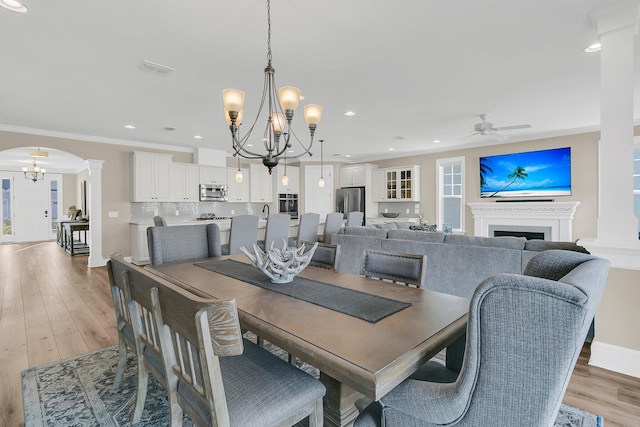 dining room with decorative columns, light wood-style floors, ceiling fan with notable chandelier, visible vents, and arched walkways