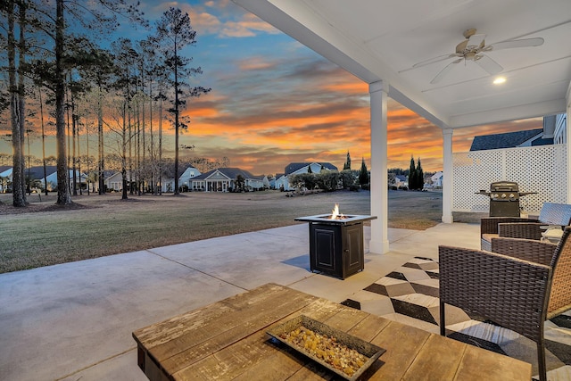 patio terrace at dusk with grilling area, a fire pit, ceiling fan, and a lawn