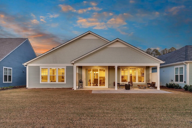back of house at dusk with a lawn and a patio area