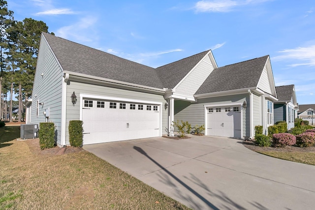 view of front of house with driveway, roof with shingles, an attached garage, a front lawn, and central AC