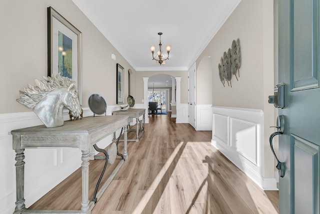 foyer entrance featuring ornamental molding, a chandelier, arched walkways, light wood-style flooring, and wainscoting