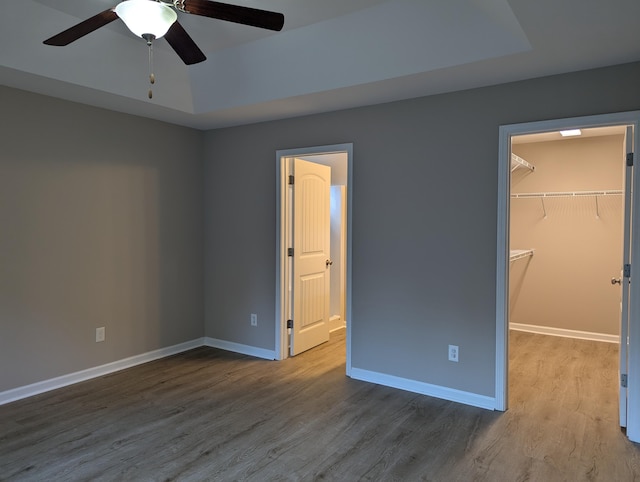 unfurnished bedroom featuring a closet, a walk in closet, hardwood / wood-style floors, and ceiling fan