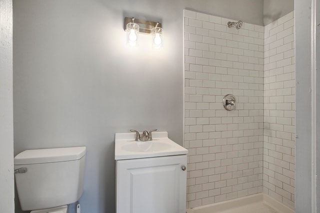 bathroom featuring a tile shower, vanity, and toilet