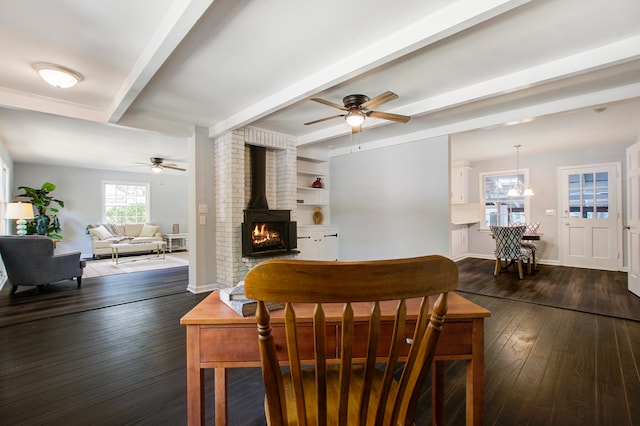 dining room featuring ceiling fan, dark hardwood / wood-style floors, beam ceiling, and a wood stove