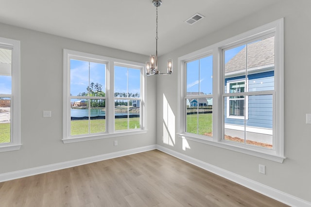 unfurnished dining area featuring visible vents, light wood-style flooring, baseboards, and a notable chandelier