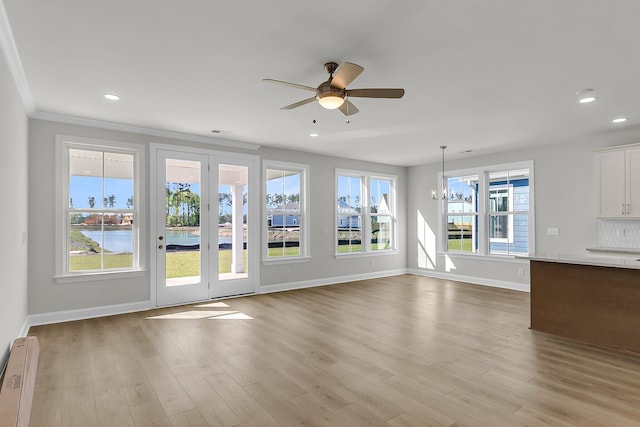 unfurnished living room featuring a baseboard heating unit, ceiling fan, a chandelier, baseboards, and healthy amount of natural light