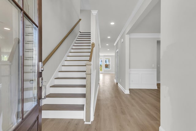 stairs featuring wood finished floors, ornamental molding, and recessed lighting