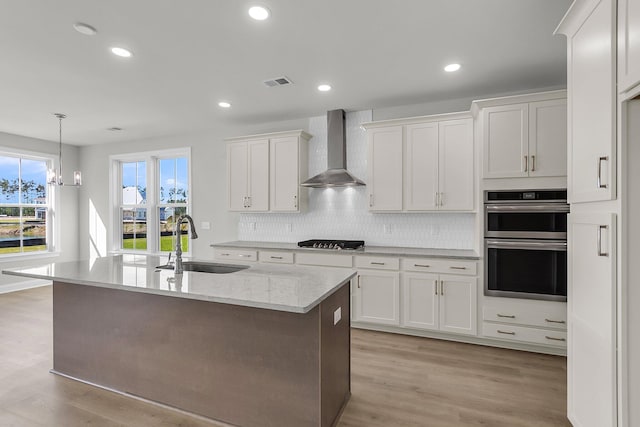 kitchen with wall chimney range hood, gas stovetop, a sink, double oven, and white cabinetry