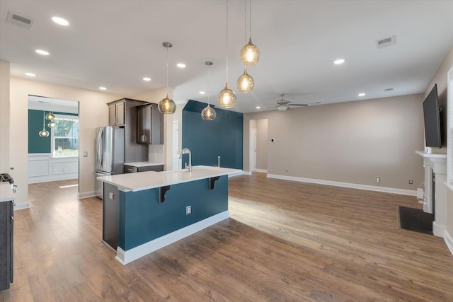 kitchen with dark brown cabinetry, ceiling fan, decorative light fixtures, a center island with sink, and a breakfast bar area