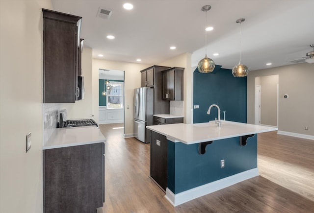 kitchen with a kitchen island with sink, stainless steel fridge, decorative light fixtures, range, and a breakfast bar area