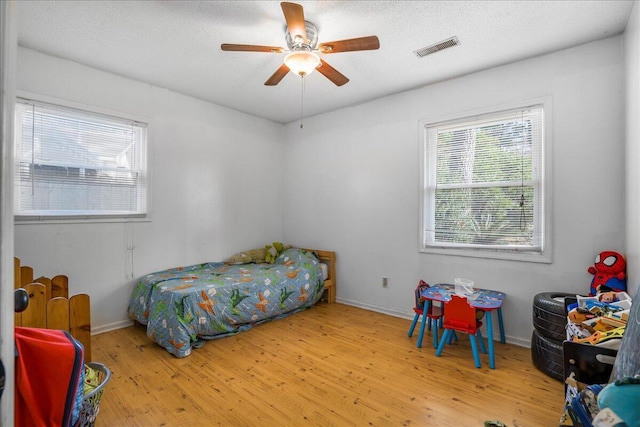 bedroom with ceiling fan, light hardwood / wood-style floors, and a textured ceiling