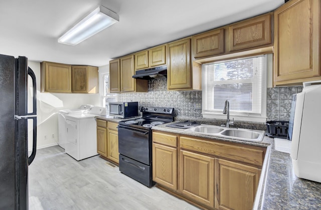 kitchen featuring under cabinet range hood, a sink, washer and dryer, decorative backsplash, and black appliances