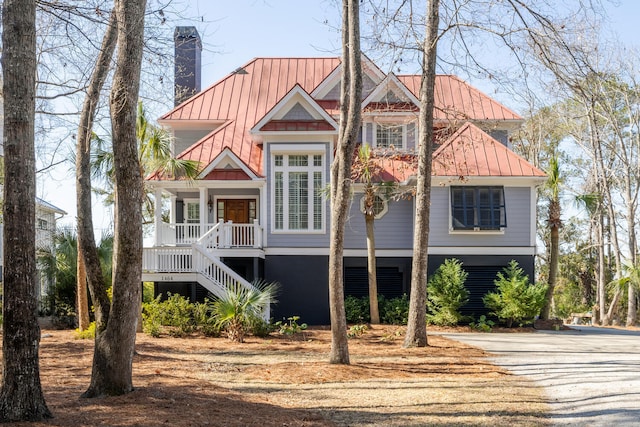 raised beach house featuring a standing seam roof, covered porch, a chimney, stairs, and metal roof