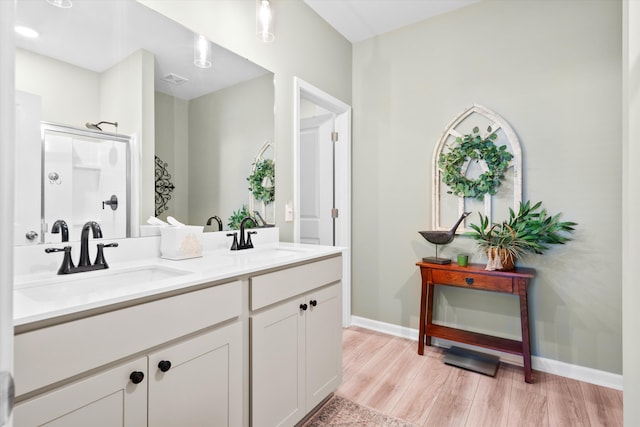 bathroom featuring double vanity, a shower with shower door, a sink, and wood finished floors