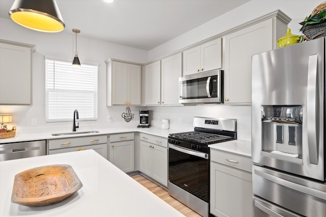 kitchen featuring light wood finished floors, stainless steel appliances, light countertops, hanging light fixtures, and a sink