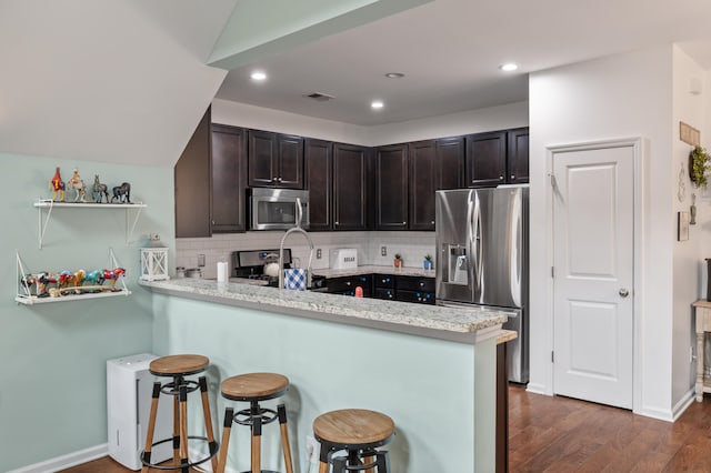 kitchen featuring decorative backsplash, kitchen peninsula, stainless steel appliances, a breakfast bar, and dark hardwood / wood-style flooring