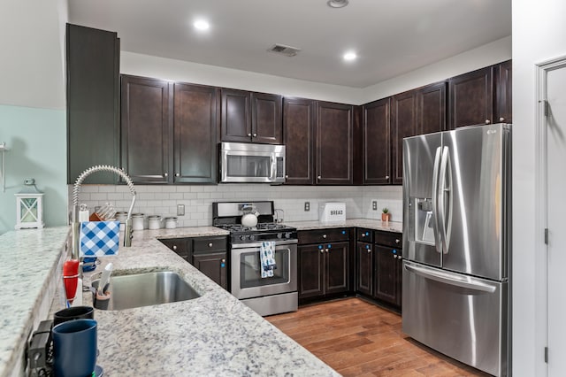 kitchen with decorative backsplash, sink, light stone countertops, appliances with stainless steel finishes, and light hardwood / wood-style floors