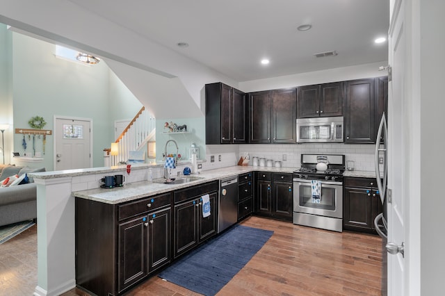 kitchen featuring kitchen peninsula, sink, dark brown cabinetry, appliances with stainless steel finishes, and light hardwood / wood-style floors