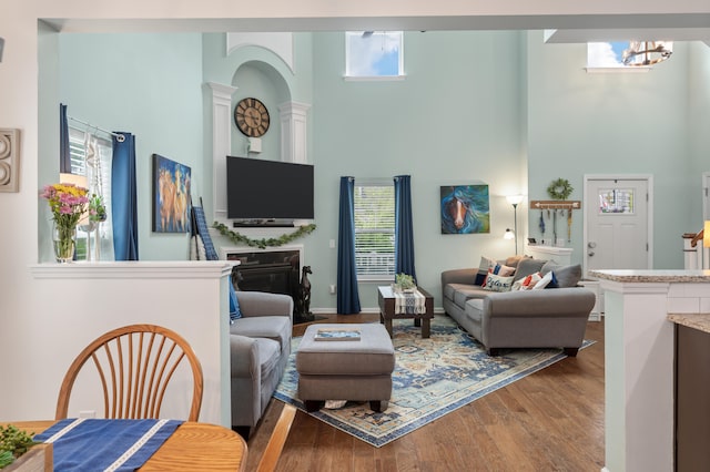 living room featuring a high ceiling, a notable chandelier, hardwood / wood-style flooring, and decorative columns