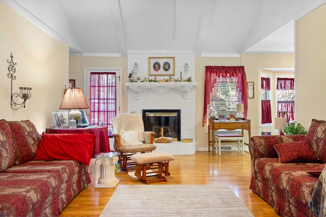 living room featuring lofted ceiling with beams, light hardwood / wood-style flooring, a fireplace, and a healthy amount of sunlight