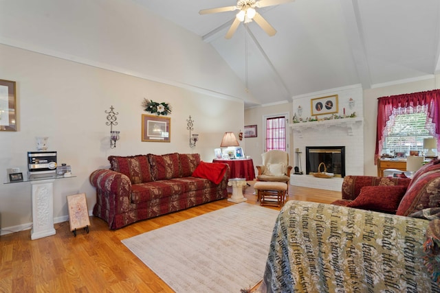 living room featuring beamed ceiling, light hardwood / wood-style flooring, a brick fireplace, high vaulted ceiling, and ceiling fan