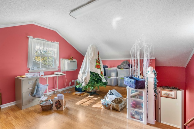 additional living space with a textured ceiling, a wall mounted AC, hardwood / wood-style flooring, and vaulted ceiling