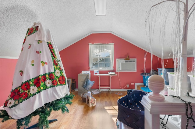 additional living space featuring a textured ceiling, vaulted ceiling, a wall mounted air conditioner, and hardwood / wood-style flooring