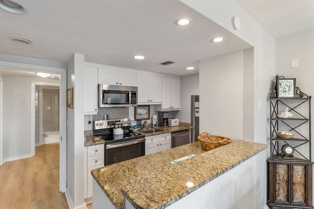 kitchen featuring light hardwood / wood-style floors, kitchen peninsula, white cabinetry, appliances with stainless steel finishes, and stone counters