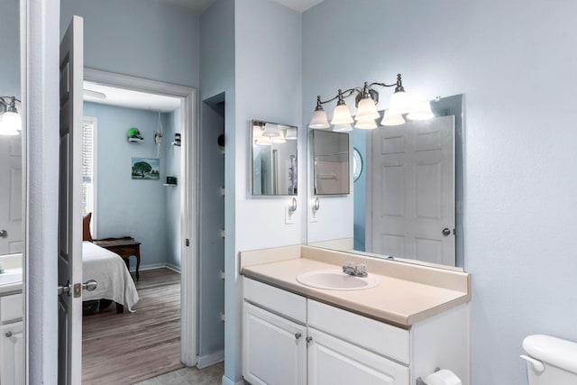 ensuite bathroom featuring vanity, connected bathroom, baseboards, and toilet