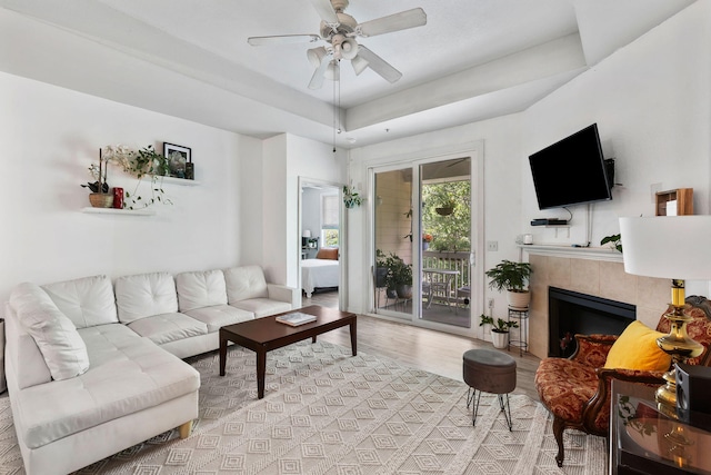 living room featuring a ceiling fan, wood finished floors, a raised ceiling, and a fireplace