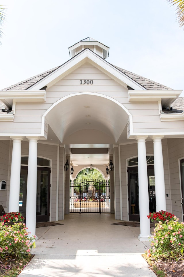 view of exterior entry featuring roof with shingles, fence, and concrete driveway
