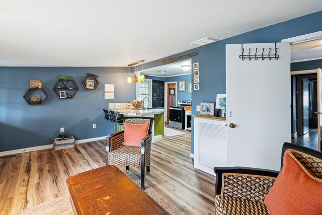 kitchen featuring hanging light fixtures, sink, light hardwood / wood-style flooring, stainless steel range with electric cooktop, and a kitchen bar