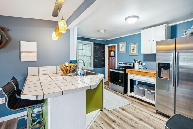 kitchen featuring pendant lighting, light hardwood / wood-style floors, tile counters, white cabinets, and appliances with stainless steel finishes