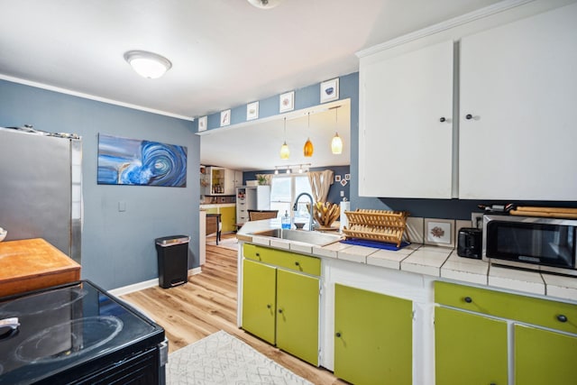 kitchen with light hardwood / wood-style floors, tile counters, sink, stainless steel appliances, and decorative light fixtures