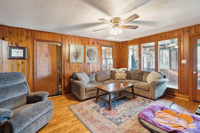 living room with a textured ceiling, light hardwood / wood-style floors, wooden walls, and ceiling fan