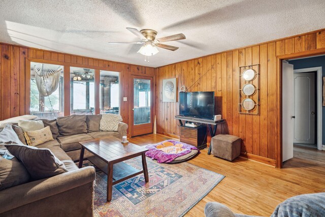 living room with a textured ceiling, wood walls, hardwood / wood-style floors, and ceiling fan