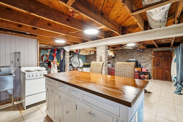 kitchen with white gas range oven, brick wall, a kitchen island, light tile patterned floors, and wood counters