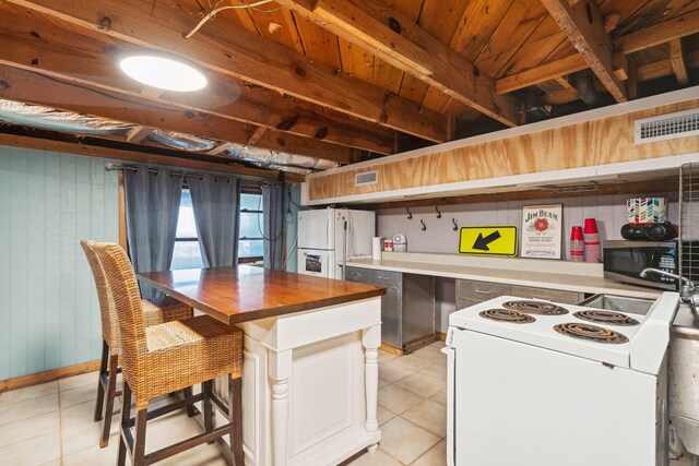 kitchen with white appliances, light tile patterned flooring, a kitchen island, and wooden counters