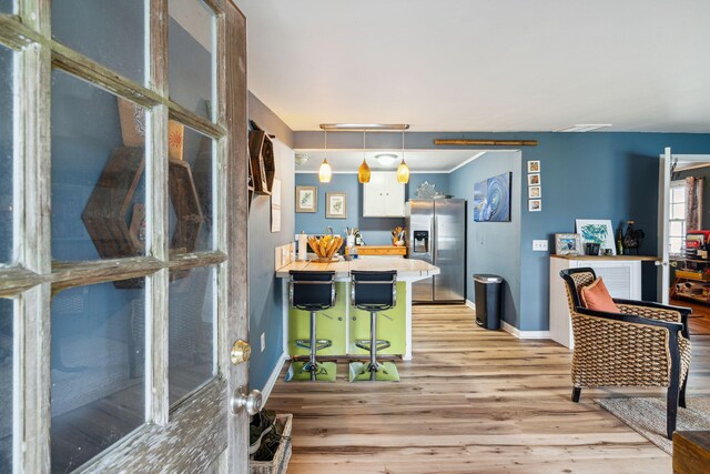 kitchen with white cabinets, decorative light fixtures, light hardwood / wood-style flooring, stainless steel fridge with ice dispenser, and a breakfast bar area