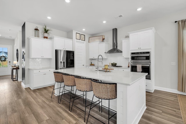kitchen featuring a breakfast bar, wall chimney exhaust hood, a sink, appliances with stainless steel finishes, and backsplash