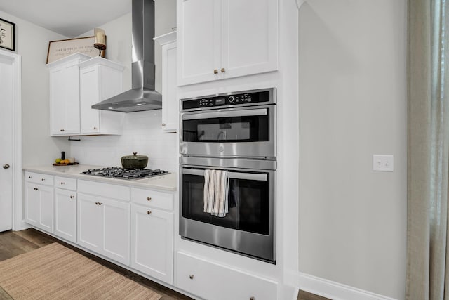kitchen with wall chimney range hood, dark wood-style flooring, appliances with stainless steel finishes, light countertops, and white cabinets