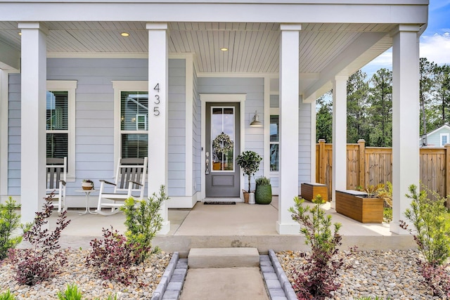 view of exterior entry with covered porch and fence