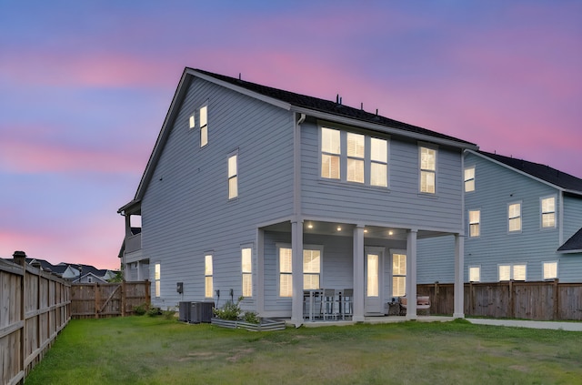 back of property at dusk featuring a fenced backyard, a patio area, central AC, and a yard