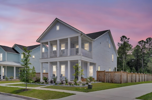 view of front of property with fence, covered porch, a lawn, and a balcony