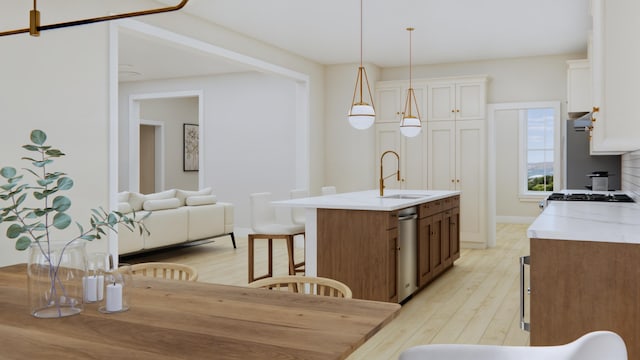 kitchen featuring a center island with sink, sink, pendant lighting, light wood-type flooring, and white cabinetry