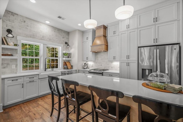 kitchen featuring open shelves, stainless steel appliances, premium range hood, a sink, and decorative backsplash